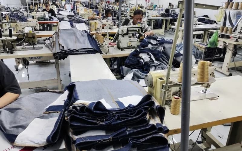 Denim sewing workshop with stacked jean panels, thread cones and sewing machines